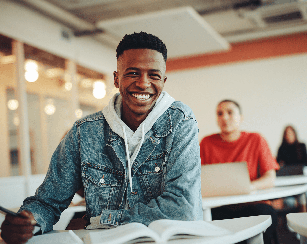 Smiling student in classroom, holding pen.